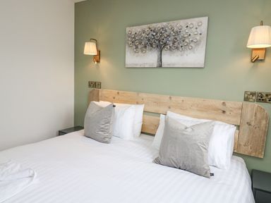 A bedroom with a bed with gray pillows white sheets a wooden headboard and wall lamps at Barcud Coch - Red Kite in Garthmyl