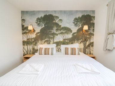 A bedroom with a double bed two decorative pillows wall lamps and tree wallpaper at Barcud Coch - Red Kite in Garthmyl