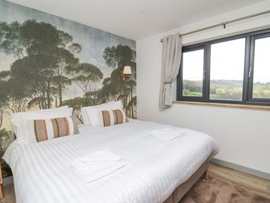 A bedroom with a double bed white bedding two pillows two towels and a window showing a rural landscape at Barcud Coch - Red Kite in Garthmyl