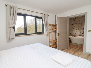 A bedroom with a bed towel rack window and an open door leading to a bathroom with a bathtub at Barcud Coch - Red Kite in Garthmyl