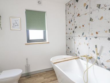 A bathroom with a white bathtub wooden floor and terrazzo tiled wall at Barcud Coch - Red Kite in Garthmyl