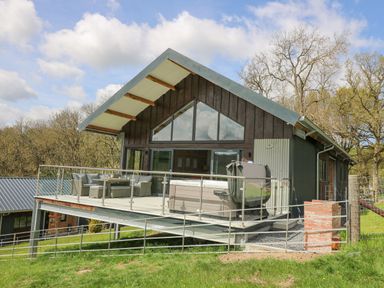 A cabin with a raised deck featuring outdoor seating and a hot tub at Barcud Coch - Red Kite in Garthmyl