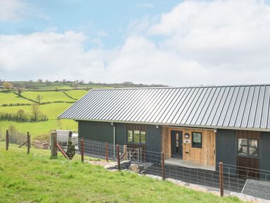 A modern barn-style building with metal roof and wooden entrance surrounded by green fields and fences at Barcud Coch - Red Kite in Garthmyl