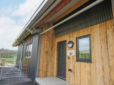 The exterior entrance of a building with wood and metal paneling and a black door at Barcud Coch - Red Kite in Garthmyl