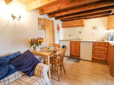A kitchen and dining area with wooden cabinets a tiled floor a small table with chairs and flowers on the table at Ty Bach Twt Synod Inn near New Quay