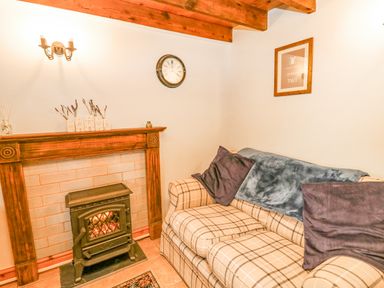A sitting room with a plaid sofa a wood-burning stove and a clock on the wall at Ty Bach Twt Synod Inn near New Quay