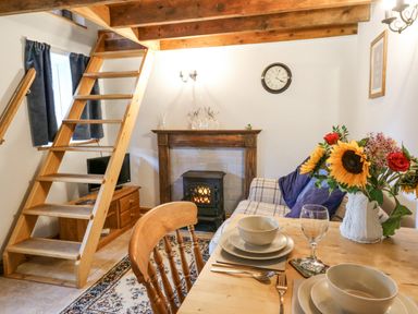 A living room with wooden stairs next to a fireplace a dining table set with dishes and a vase of flowers at Ty Bach Twt Synod Inn near New Quay