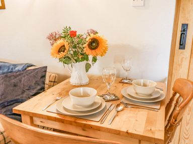 A dining table set for two with bowls plates cutlery glasses and a vase with sunflowers at Ty Bach Twt in Synod Inn near New Quay