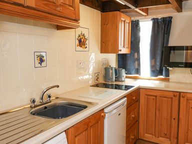 A kitchen with wooden cabinets a sink kettle toaster and microwave at Ty Bach Twt in Synod Inn near New Quay