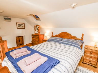 A bedroom with a wooden bed with striped bedding two bedside tables with lamps a wooden chest of drawers and folded towels on the bed at Ty Bach Twt in Synod Inn near New Quay