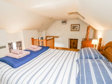 A bedroom with a double bed striped bedding wooden headboard bedside lamp and wooden furniture at Ty Bach Twt Synod Inn near New Quay