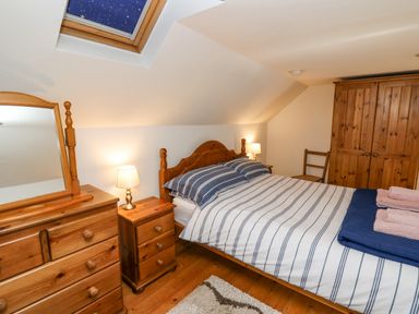 A bedroom with a double bed two bedside tables lamps a dresser with mirror a wardrobe and a chair at Ty Bach Twt in Synod Inn near New Quay