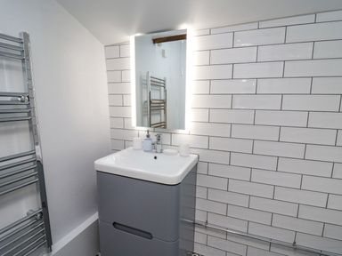 A bathroom sink with a lit mirror above it and a chrome towel radiator at Ty Bach Twt Synod Inn near New Quay