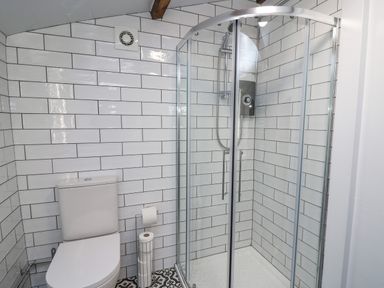 A bathroom with a toilet and glass shower enclosure with white tiled walls at Ty Bach Twt in Synod Inn near New Quay