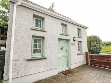 Exterior of a small house with four windows and a door with a doormat at Ty Bach Twt in Synod Inn near New Quay