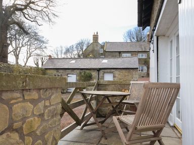 A stone patio with wooden chairs and table outside a building at Harness Lodge in Seahouses