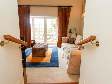 A sitting room with a beige sofa a wicker coffee table and glass doors with orange curtains at Harness Lodge in Seahouses