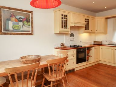 A kitchen with wooden chairs and table a wooden bowl a stove and cream cabinets at Harness Lodge in Seahouses