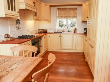 A kitchen with wooden floor cream cabinets gas stove oven wooden table and chairs at Harness Lodge in Seahouses