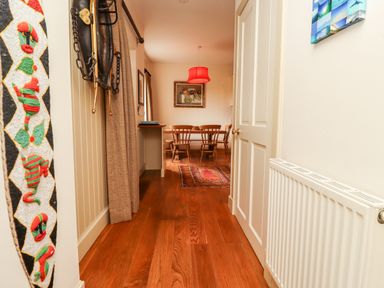 A hallway with wooden floor leading to a dining area with wooden chairs and table and a red lampshade at Harness Lodge in Seahouses