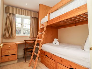 A bedroom with a wooden bunk bed a desk a chair and a window with striped curtains at Harness Lodge in Seahouses