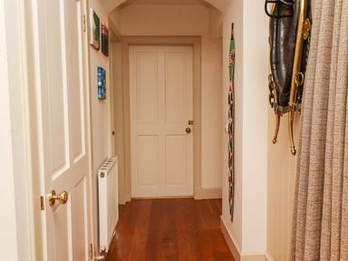 A hallway with a wooden floor white doors a radiator and decorative items on the walls at Harness Lodge in Seahouses