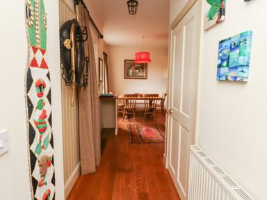 A hallway with wooden floor leading to a dining area with a wooden table and chairs and a red hanging lamp at Harness Lodge in Seahouses