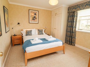 A bedroom with a double bed two pillows two rolled towels bedside table with lamp framed pictures wardrobe window with curtains at Harness Lodge in Seahouses