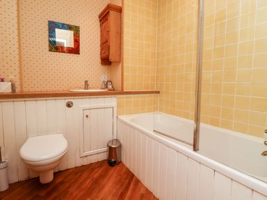 A bathroom with a toilet bathtub sink mirror wooden cabinet and patterned wallpaper at Harness Lodge in Seahouses