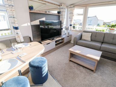 A living room with a gray sofa a wooden coffee table a TV on a stand and a dining table with two blue stools at 17 Summer Meadows in Ashington
