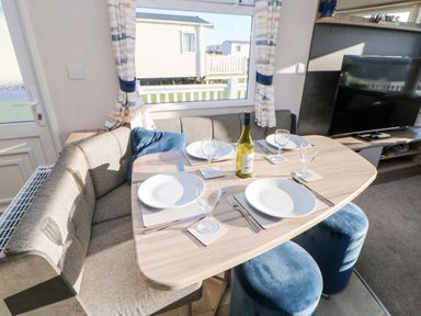 A dining area with a wooden table set for four with plates glasses cutlery a bottle and blue stools at 17 Summer Meadows in Ashington