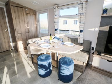 A dining area with a wooden table set for four people with blue stools and a built-in bench at 17 Summer Meadows Ashington