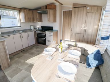 A kitchen and dining area with wooden cabinets a stove a dining table set for four and a cushioned bench at 17 Summer Meadows in Ashington