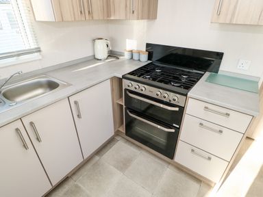 A kitchen corner with a sink, kettle, jars, stove, and cabinets at 17 Summer Meadows Ashington