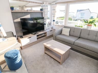 A living room with a grey sofa a wooden coffee table television and windows showing outside at 17 Summer Meadows in Ashington