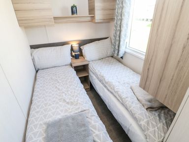 A bedroom with two single beds with patterned bedding and towels a small bedside table with a lamp a window and wooden cabinets at 17 Summer Meadows in Ashington