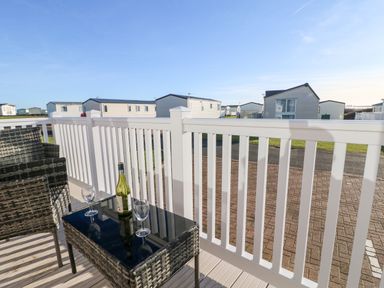 A balcony with wicker chairs and a table with a wine bottle and glasses overlooking static caravans at 17 Summer Meadows in Ashington