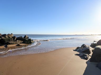 A sandy beach with rocks along the shore and ocean waves at 17 Summer Meadows in Ashington