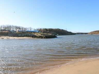 A river with boats on the shore and a bridge in the distance at 17 Summer Meadows in Ashington