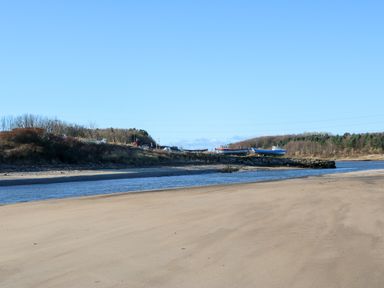 A sandy beach with a narrow river and boats on the shore in a rural area at 17 Summer Meadows in Ashington