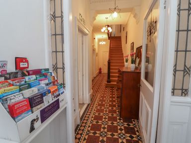 A hallway with a patterned tiled floor a chest of drawers with vases and flowers stairs and a brochure stand at The Furness Haven in Barrow-In-Furness