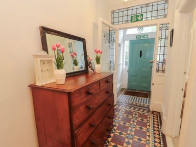 A hallway with a wooden chest of drawers a mirror vases with flowers and a blue door at The Furness Haven in Barrow-In-Furness