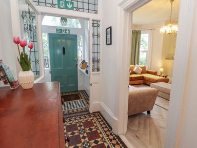 An entrance hallway with a teal door and patterned tile floor leading to a living room with a brown sofa and armchair at The Furness Haven in Barrow-In-Furness
