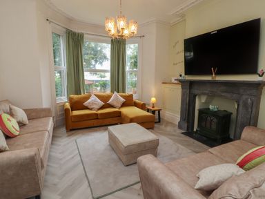 A living room with couches a ottoman and a television above a fireplace at The Furness Haven in Barrow-In-Furness