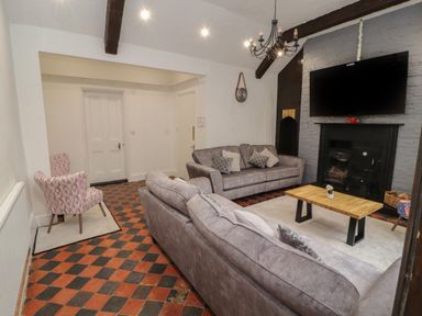 A living room with two grey sofas a wooden coffee table a TV above a fireplace and a patterned armchair at The Furness Haven in Barrow-In-Furness