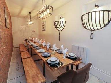 A dining room with a long wooden table set with plates and napkins and benches along a brick wall at The Furness Haven in Barrow-In-Furness