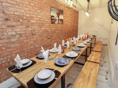 A dining room with a long wooden table set with plates bowls glasses and napkins along a brick wall at The Furness Haven in Barrow-In-Furness