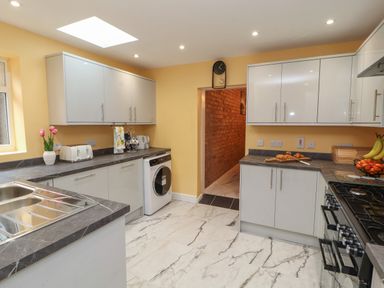 A kitchen with white cabinets grey countertops a washing machine a stove and a sink with a window at The Furness Haven in Barrow-In-Furness