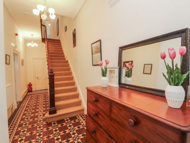 A hallway with a staircase a wooden dresser with a mirror and vases with tulips on top at The Furness Haven in Barrow-In-Furness