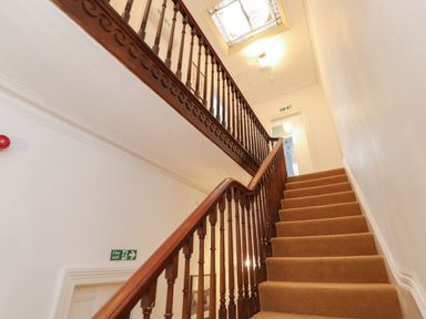 A carpeted staircase with wooden banister and white walls in a building hallway at The Furness Haven in Barrow-In-Furness